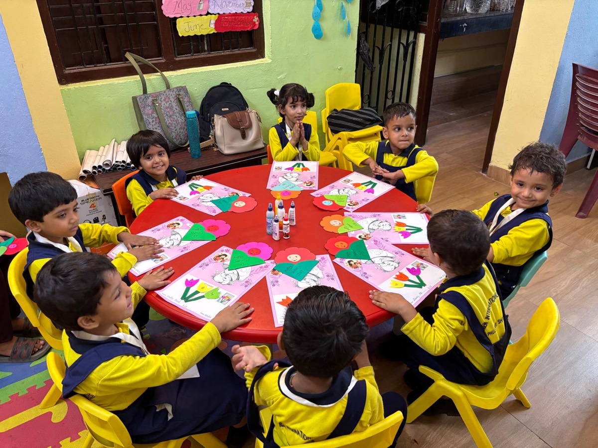 Children seated around a red table making paper craft decorations together