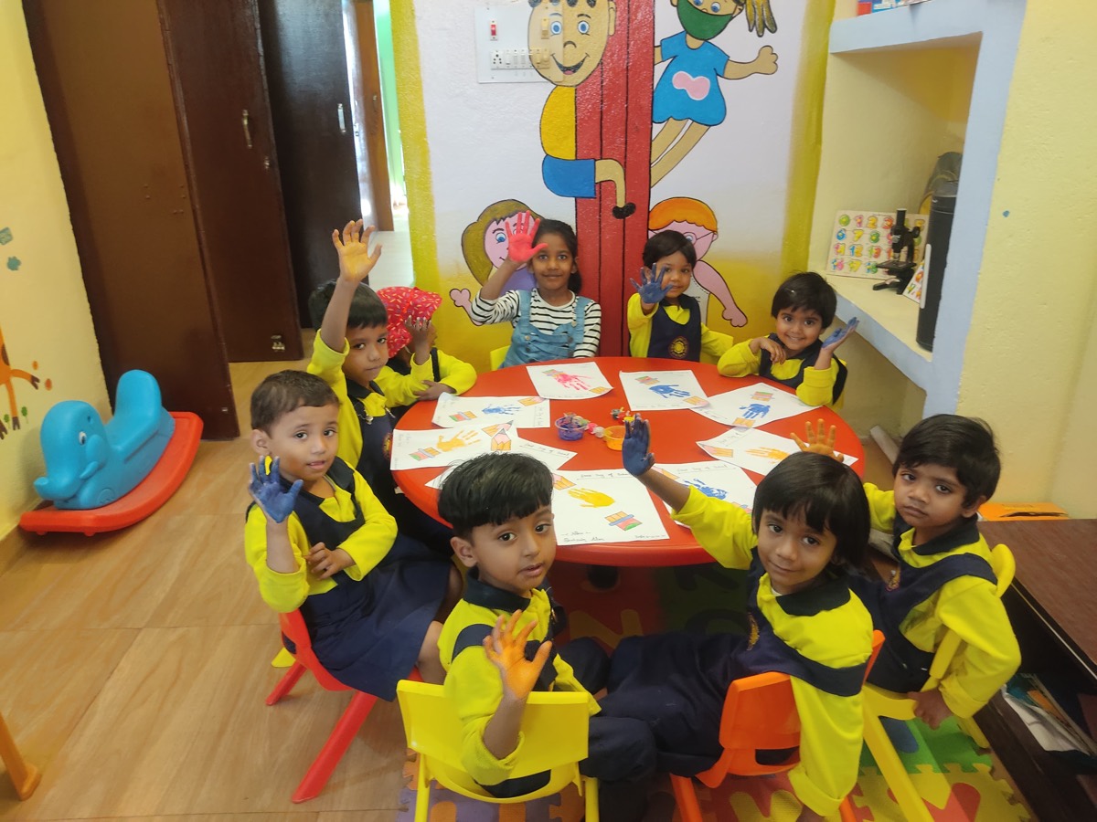 Children at a table showing their paint-covered hands during finger painting