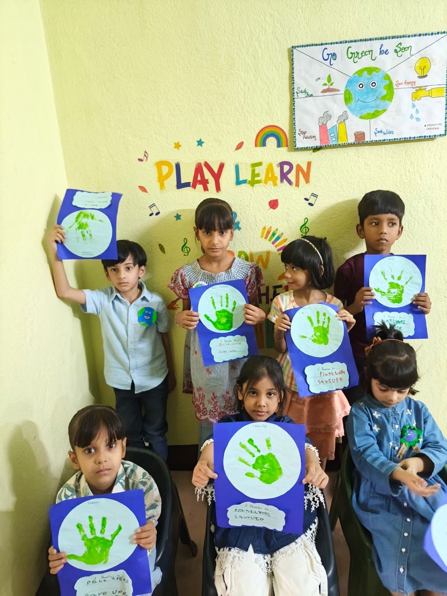 Children holding green handprint artwork below a Play Learn wall display