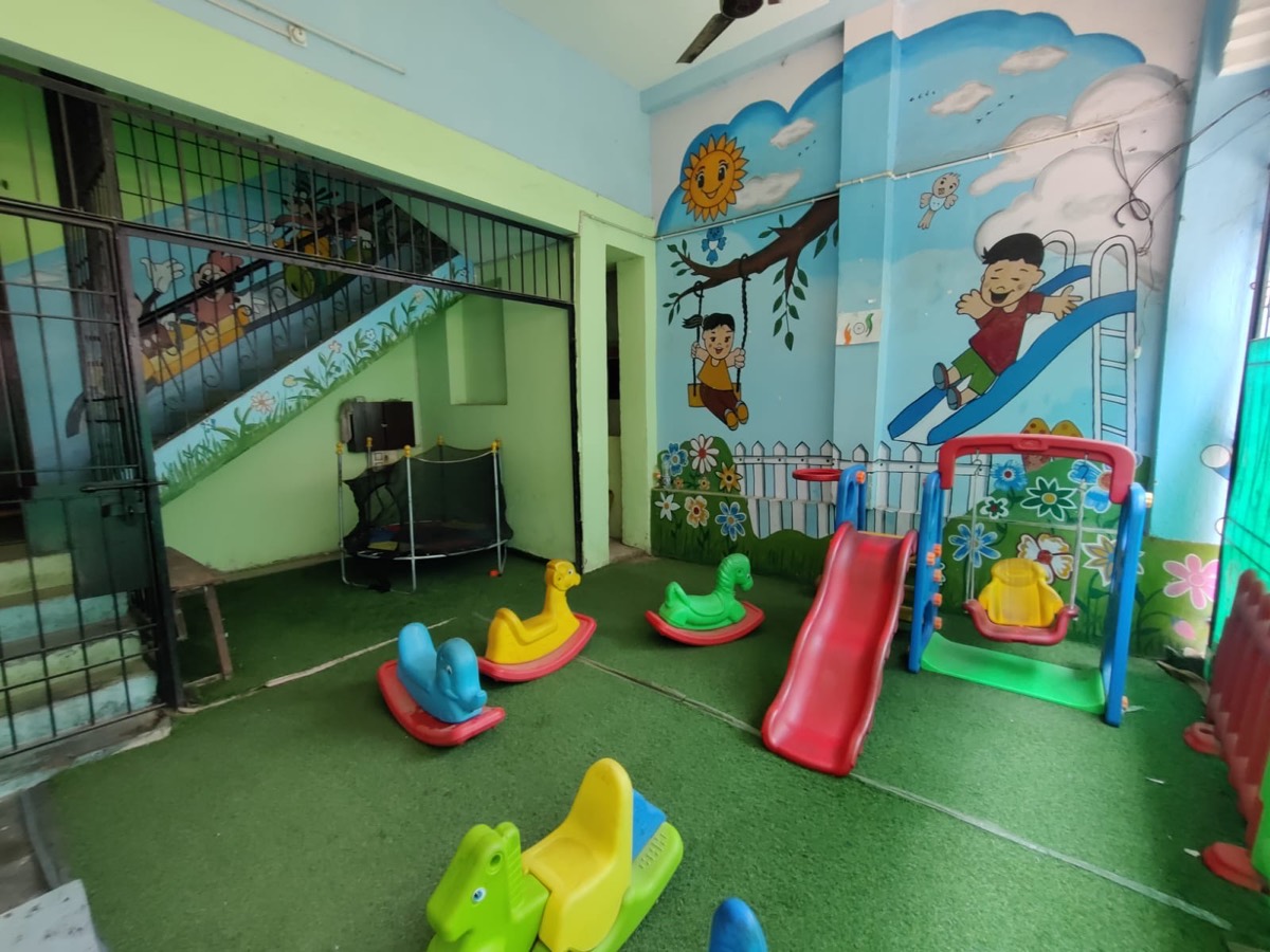 The indoor play area with a slide, swing, rockers and trampoline on artificial grass
