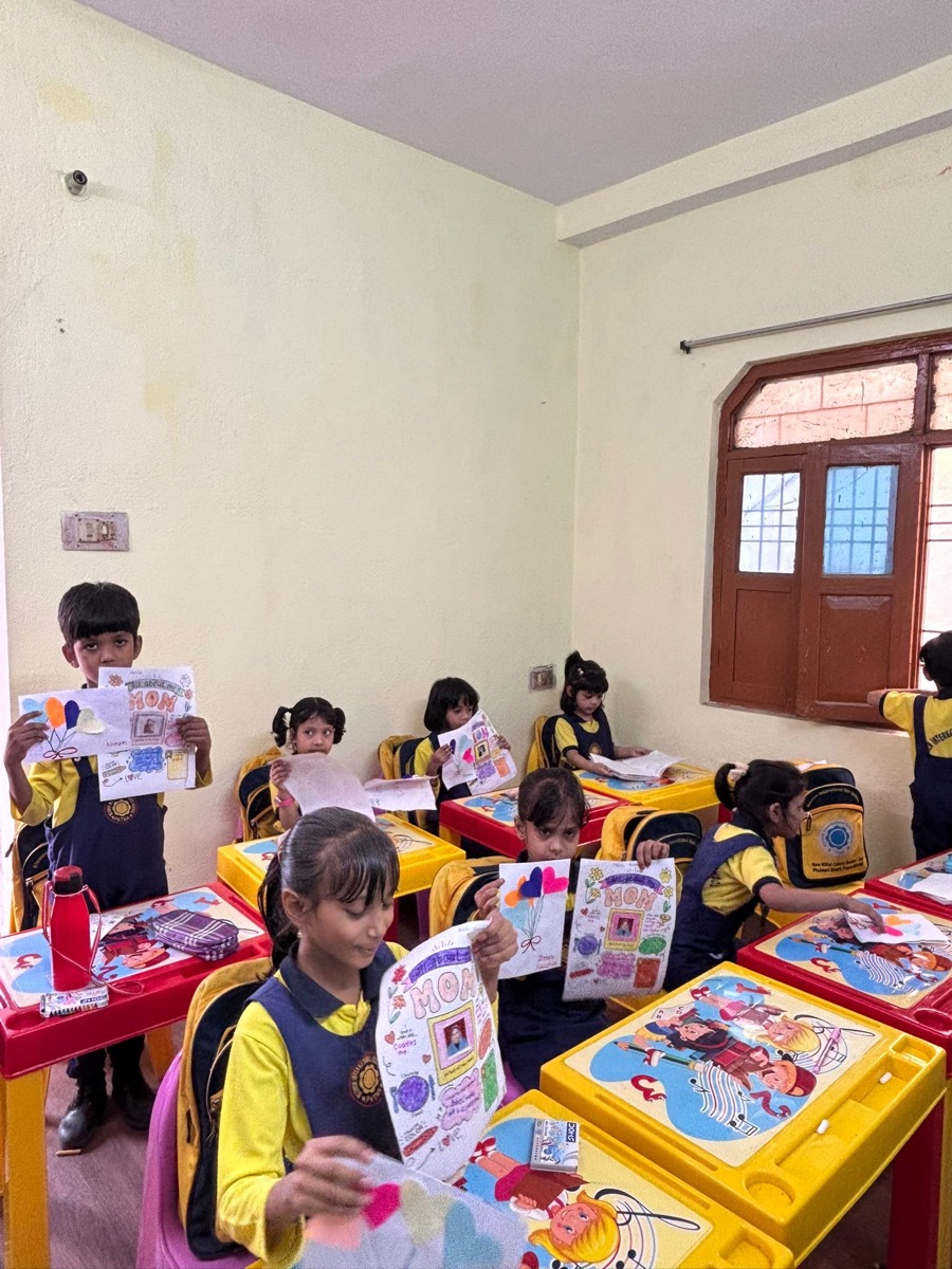 Children at their desks holding up hand-made Mother's Day cards they have drawn and coloured